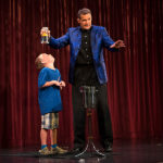 [Photo: A volunteer from the audience looks nervously up at a glass of water, suspended upside down over his head by the magician Rick Wilcox.]